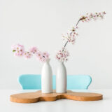 Two white vases with delicate pink flowers on a wooden tray.