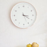 A white wall clock showing 3:17 with two small pumpkins below it.