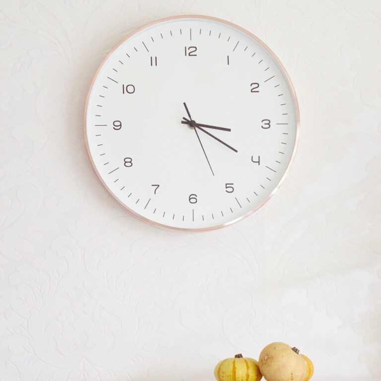 A white wall clock showing 3:17 with two small pumpkins below it.